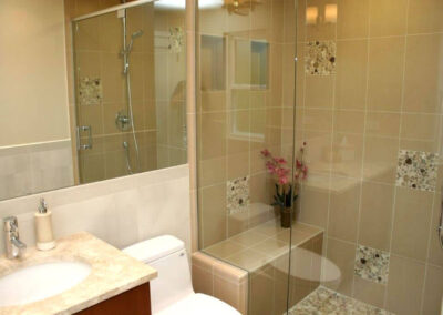 Remodel of a small bathroom to make it appear more spacious and open with glass and lighter colors.