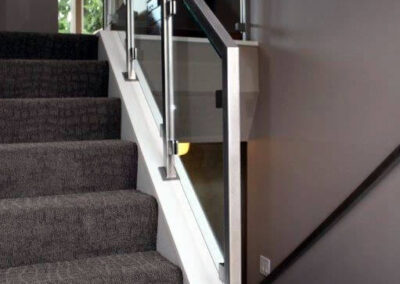 A custom designed and built railing using glass and metal open up the narrow and dark split entry.